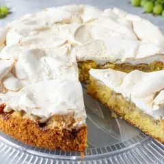 Ein köstlicher Stachelbeer Baiser Kuchen mit goldbraunem Boden und fluffiger Baiserhaube, ein Stück ist bereits angeschnitten.