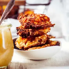 Goldbraune Kartoffelpuffer stapeln sich in einer Schüssel, daneben ein Glas Apfelmus. Ein perfektes Kartoffelpuffer Rezept für jeden Anlass.