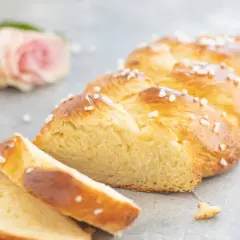 Ein goldbrauner Hefezopf, bestreut mit Hagelzucker, liegt angeschnitten auf grauem Untergrund. Ein tolles Rezept für Hefezopf!