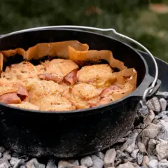 Ein Gusseisentopf mit einem leckeren Crumble, der über glühender Kohle für das **Winter grillen** zubereitet wird.