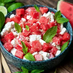 Erfrischender sommerlicher Melonensalat mit Feta und Minze, garniert mit Limettenspalten und einem Holzlöffel.