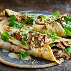 Herzhafte Pfannkuchen gefüllt mit Pilzen, garniert mit Nüssen und frischen Kräutern, übergossen mit cremiger Sauce.