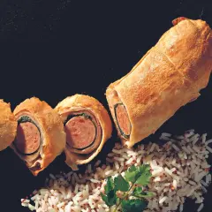 Herzhaft belegter Bratwurst im Teigmantel, aufgeschnitten und mit Reis garniert.