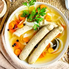 Herzhaftes rezept blaue zipfel: zwei Würste in Brühe mit Karotten, Zwiebeln und Petersilie.