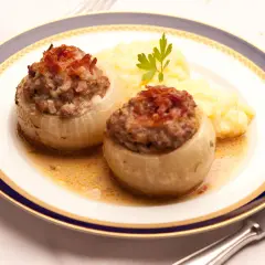 Zwei gefüllte Bamberger Zwiebeln mit Hackfleisch und Speck, serviert mit Kartoffelpüree auf einem Teller mit blau-goldener Bordüre.