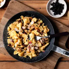Kaiserschmarrn-Rezepte: Ein goldbrauner Kaiserschmarrn mit Mandelsplittern, Rosinen und Apfelstücken in einer Pfanne, bestäubt mit Puderzucker.
