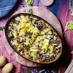 Herzhafter kartoffelauflauf mit hackfleisch, überbacken mit Käse und garniert mit Petersilie. Dazu frische Kartoffeln, Lauch und ein Stück Käse.