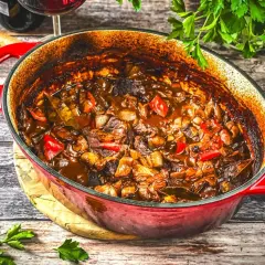 Herzhaftes Gulasch-Rezept in einem roten Bräter, mit zarten Fleischstücken, Paprika und Zwiebeln, bereit zum Servieren.
