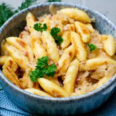 Herzhafte Bubespitzle mit Sauerkraut und Speck, garniert mit Petersilie, in einer blauen Schüssel.