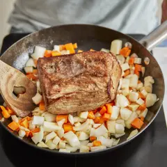 Ein gebratener Rinderbraten ruht auf gewürfeltem Wurzelgemüse in einer Pfanne. Perfekt für ein herzhaftes rinderbraten rezept.