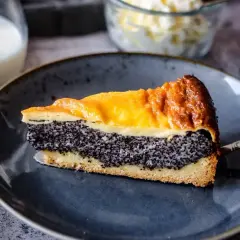 Ein Stück Mohn Schmand Kuchen mit goldbrauner Kruste und saftiger Mohnfüllung auf einem blauen Teller.
