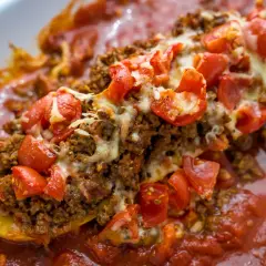 Herzhafte zucchini schiffchen gefüllt mit Hackfleisch, Tomaten und Käse, in einer roten Sauce.