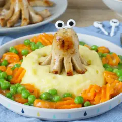 Ein lustiger Tintenfisch aus Bratwurst vom Vortag, der aus Kartoffelbrei mit Erbsen und Karotten schaut.