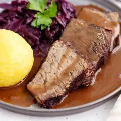 Original Sauerbraten: zartes Rindfleisch in dunkler Sauce, serviert mit Rotkohl und Klößen.