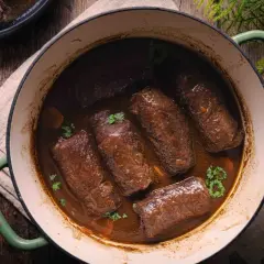 Rinderrouladen im Backofen schmorend in dunkler Sauce, garniert mit Petersilie. Ein rustikales Gericht, das Wärme und Genuss verspricht.