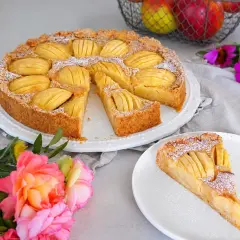 Ein sensationelles Apfeltarte-Rezept: goldbrauner Boden, saftige Äpfel, Puderzucker. Daneben eine Rose und Äpfel im Korb.