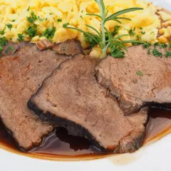 Fertig eingelegter Sauerbraten zubereiten: Zarte Scheiben Rindfleisch in dunkler Sauce mit Spätzle und Rosmarin garniert.
