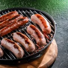 Mehrere rohe Bratwürste braten auf einem Grill. Sie sind noch nicht ganz durch, aber schon schön gebräunt.