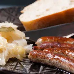 Herzhafte Bratwurst mit Sauerkraut und Brot auf dunklem Teller, bereit zum Genuss.