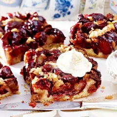 Saftige Pflaumenstücke auf einem lockeren Teig, bestreut mit Streuseln. Ein Stück gesunder Pflaumenkuchen mit einem Klecks Sahne.