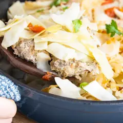 Ein Holzlöffel hebt eine Portion Krauttopf mit Hackfleisch aus einem Topf. Das Gericht ist im Ofen gebacken und mit Petersilie garniert.