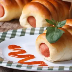 Leckere Bratwurst im Schlafrock, garniert mit einem Blatt, auf einem Teller mit Ketchup-Spur.