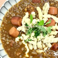 Herzhafte Linsen mit würzigen "Spotzen" (Spätzle) und Fleischwurststücken, garniert mit frischen Kräutern.