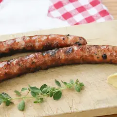 Zwei gegrillte Wildbratwürste auf einem Holzbrett mit Senf und Kräutern. Das beste Wildbratwurst Rezept für einen besonderen Genuss.