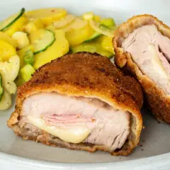 Zwei goldbraune Cordon-bleu-Schnitzel mit geschmolzenem Käse und Schinken, serviert mit einem Kartoffel-Zucchini-Salat.