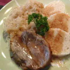 Ein Teller mit tschechischem Schweinebraten, Sauerkraut und Knödeln, garniert mit Petersilie.