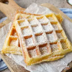 Zwei fluffige Waffeln, bestäubt mit Puderzucker, auf einem Holzbrett. Ein perfektes Rezept für fluffige Waffeln!