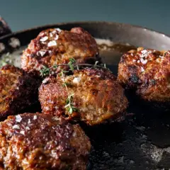 Saftige vegetarische Frikadellen braten in einer Pfanne, bestreut mit grobem Salz und frischem Thymian.