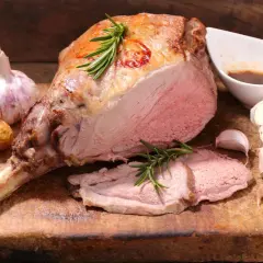 Ein saftiger Lammbraten, perfekt für Ostern, mit Rosmarin, Knoblauch und kleinen Kartoffeln auf einem Holzbrett.