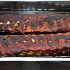 Zwei Reihen saftiger spareribs im backofen, mit einer dunklen, karamellisierten Kruste, ruhen auf einem Rost in einer Bratpfanne.
