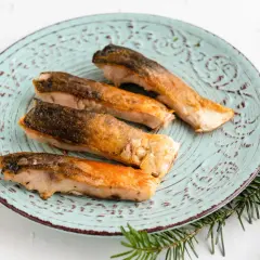 Vier goldbraun gebratene Karpfenfilets mit Haut liegen auf einem mintgrünen Teller.