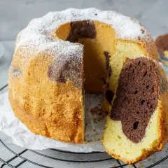 Ein saftiger Marmorkuchen, bestäubt mit Puderzucker, zeigt seine köstliche Maserung. Ein Stück wurde bereits entnommen, was ihn zum besten Marmorkuchen macht.
