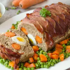 Fertiger Braten mit Speckmantel, gefüllt mit Ei und Karotten. Die Zubereitung Hase ist ein Genuss, serviert mit Erbsen und Karotten.