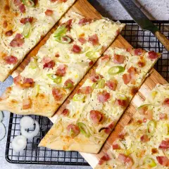 Flammkuchen-Rezept: knuspriger Teig mit Speck, Zwiebeln und Frühlingszwiebeln, bereit zum Genießen.