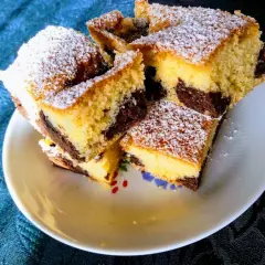 Ein saftiger versunkener Streuselkuchen mit Marmormuster, bestäubt mit Puderzucker, liegt auf einem Teller.