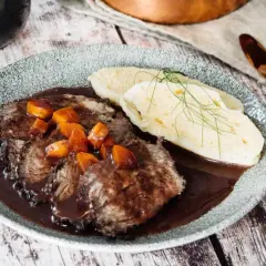 Klassisches Sauerbraten Rezept im Backofen: Zartes Rindfleisch in dunkler Soße mit Karotten und Klößen, garniert mit Dill.