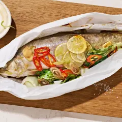 Ein ganzer Saibling, zubereitet in Papier mit Zitrone, Chili und Kräutern. Dazu eine Schale mit Dip. Perfekt zum Saibling essen.