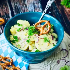 Klassisches Rezept Kartoffelsalat mit roten Zwiebeln und Petersilie, garniert mit einem Brezel.
