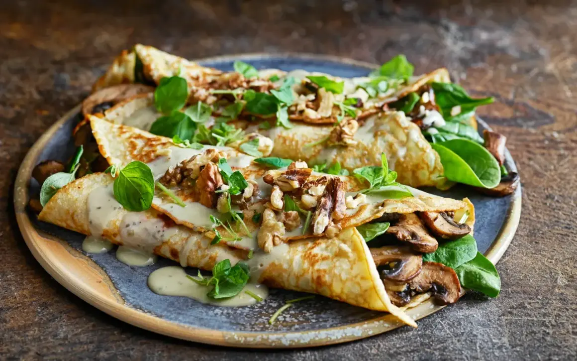 Herzhafte Pfannkuchen gefüllt mit Pilzen, garniert mit Nüssen und frischen Kräutern, übergossen mit cremiger Sauce.