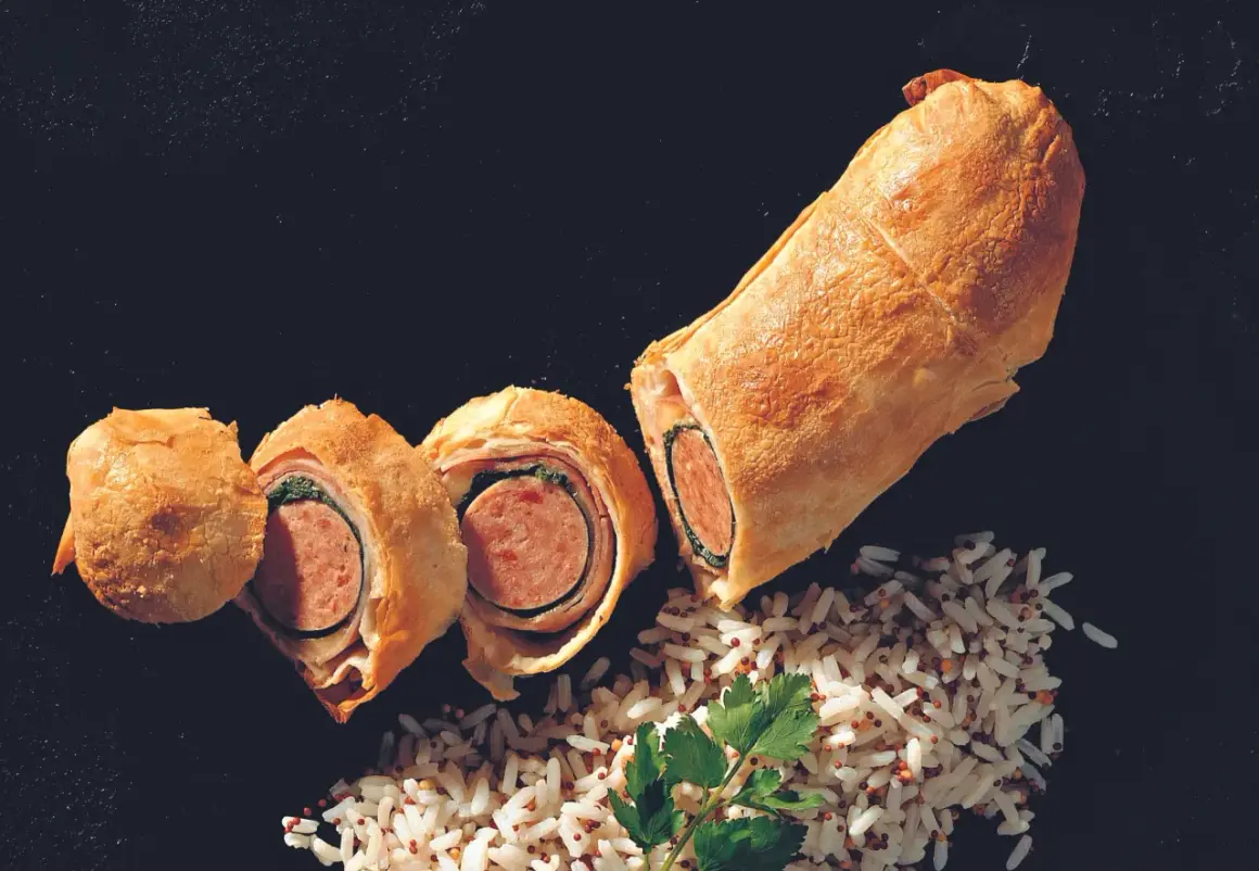 Herzhaft belegter Bratwurst im Teigmantel, aufgeschnitten und mit Reis garniert.