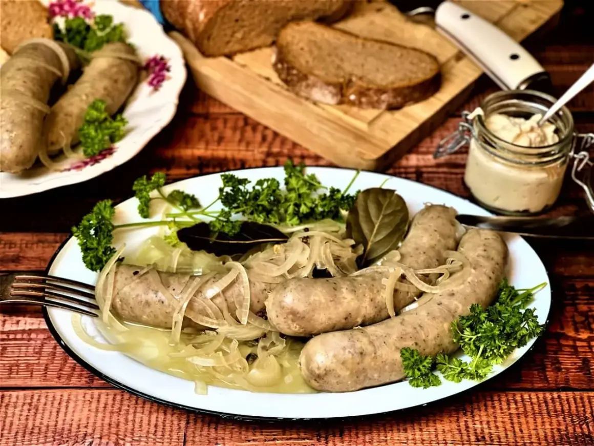 Saure Bratwurst mit Zwiebeln und Petersilie auf einem Teller, dazu Brot und ein Glas Senf.