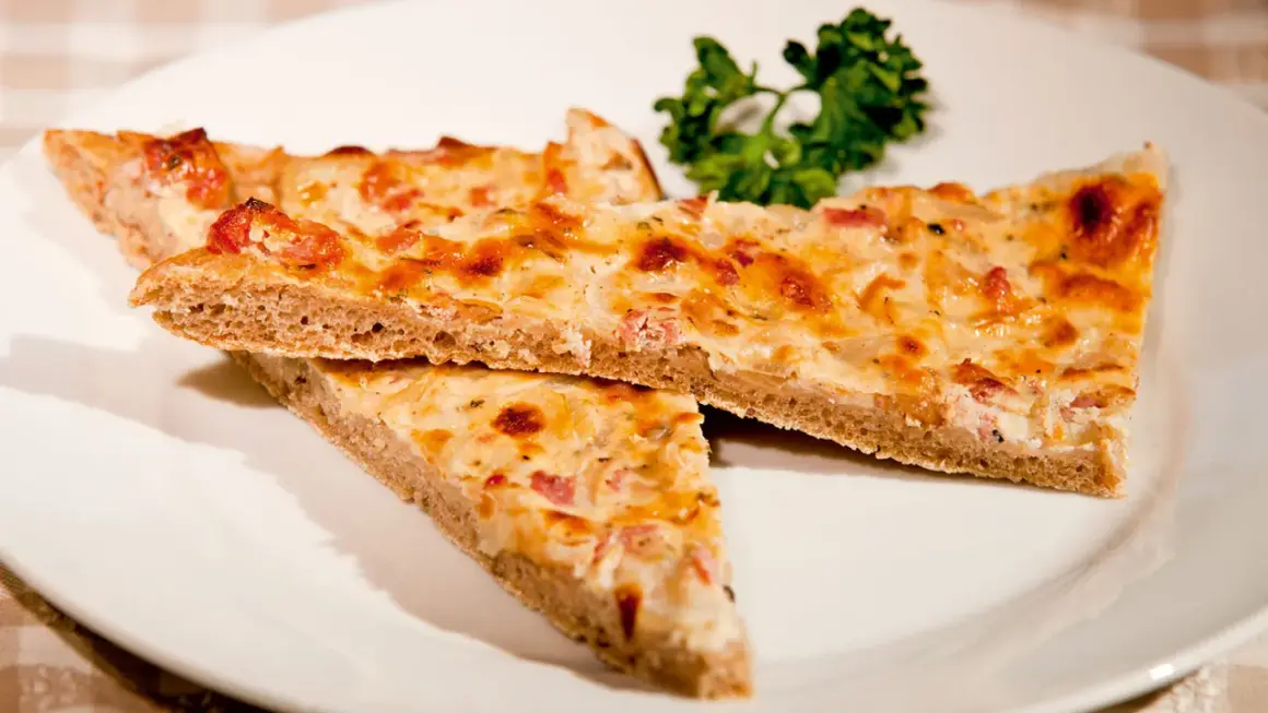 Drei Stücke herzhafter Blooz mit Speck und Zwiebeln auf einem Teller, garniert mit Petersilie. Ein köstliches Blooz-Rezept.