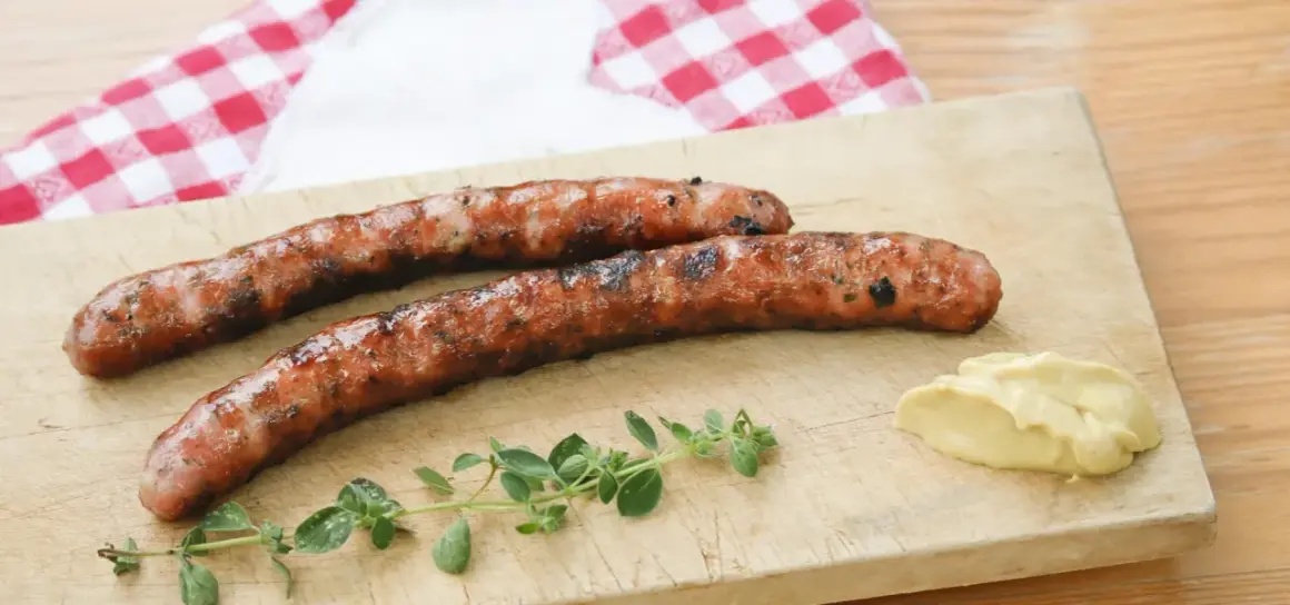 Zwei gegrillte Wildbratwürste auf einem Holzbrett mit Senf und Kräutern. Das beste Wildbratwurst Rezept für einen besonderen Genuss.