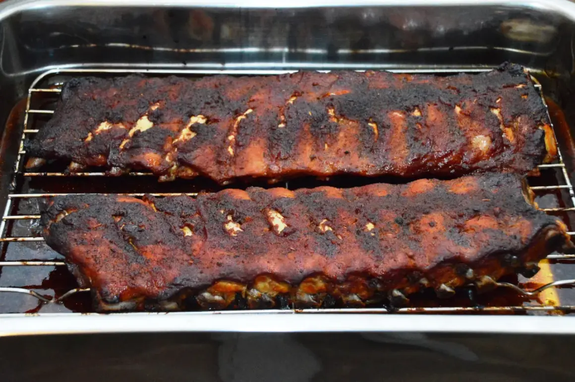 Zwei Reihen saftiger spareribs im backofen, mit einer dunklen, karamellisierten Kruste, ruhen auf einem Rost in einer Bratpfanne.