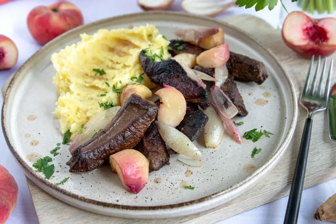 Leber braten ohne Mehl: zarte Leberstücke mit karamellisierten Zwiebeln und Pfirsichspalten, serviert mit cremigem Kartoffelpüree und frischer Petersilie.