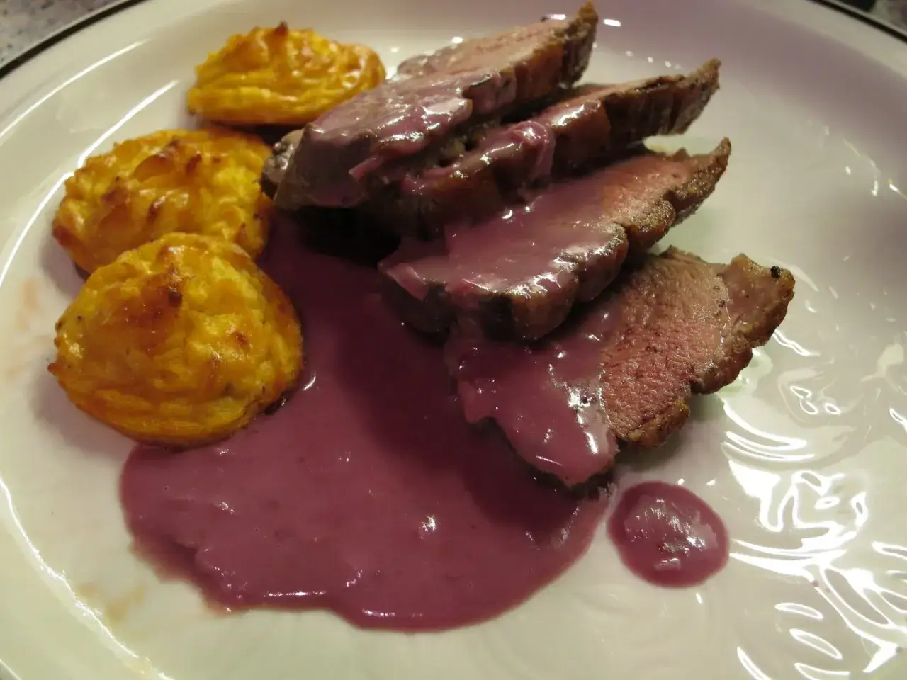 Gegrilltes Fleisch mit lila Sauce und Kartoffel-Püree-Törtchen. Ein köstliches Gericht, das an Schlehen Rezepte erinnert.
